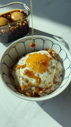 a bowl filled with rice covered in an egg and sauce next to another bowl full of eggs