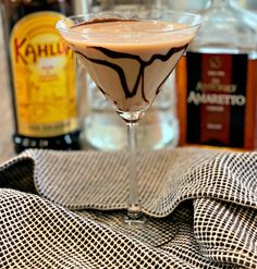 a drink in a martini glass with chocolate drizzled on the rim, next to liquor bottles