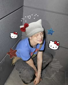 a young boy sitting on the ground wearing a hello kitty hat