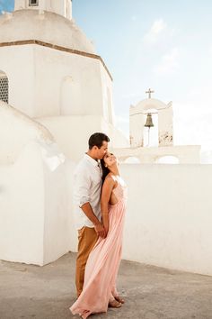 a man and woman standing next to each other in front of a white building with a bell tower