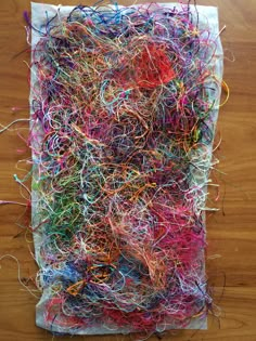 a pile of colorful yarn sitting on top of a wooden table next to a piece of paper