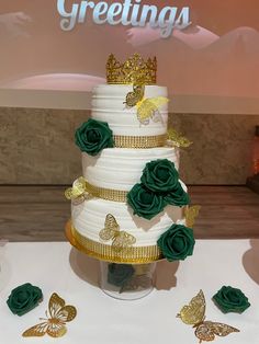 a three tiered cake with green roses and gold butterflies on the table next to it