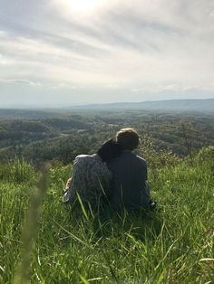 two people are sitting in the grass looking at the valley