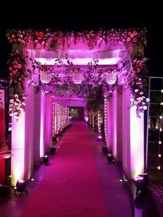 an outdoor wedding venue decorated with purple lighting and flowers on the aisle, surrounded by white pillars