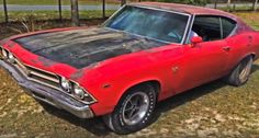 an old red car sitting in the grass