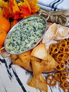 a platter filled with dip surrounded by pretzels, crackers and pumpkins