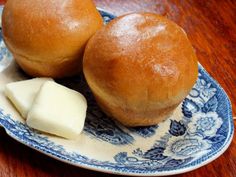 two rolls on a blue and white plate next to a piece of buttered cheese