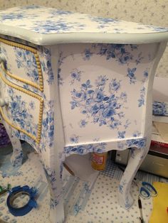 a blue and white dresser with flowers on it's side, surrounded by other items