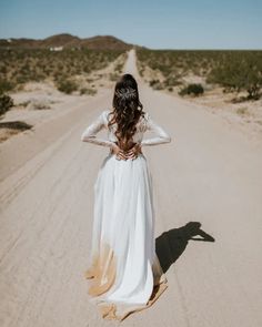 a woman in a white dress walking down a dirt road with her back to the camera