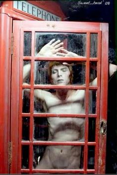 a man standing in front of a red phone booth with his hands on his head