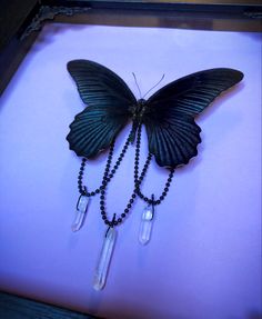 a black butterfly with long chain attached to it's wings and two clear beads