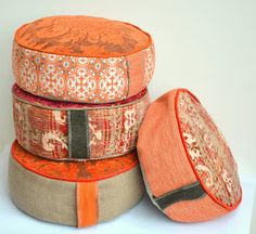 three orange and grey round cushions stacked on top of each other, one with an intricate design