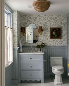 a white toilet sitting next to a sink in a bathroom under a mirror and light fixture