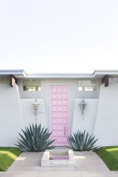 a pink door in front of a white stucco house with green grass and plants around it