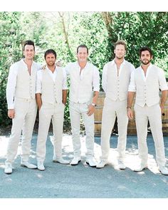 four men in white tuxedos are posing for a photo with wine barrels behind them