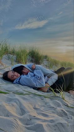 two people laying in the sand with their arms around each other