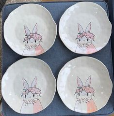 four white plates with pink bunny ears and flowers on them are sitting on a blue tray