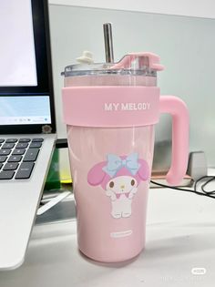 a pink cup sitting on top of a desk next to a laptop