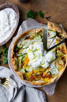 a pizza with cheese, cucumbers and sour cream on top is being cut by a knife