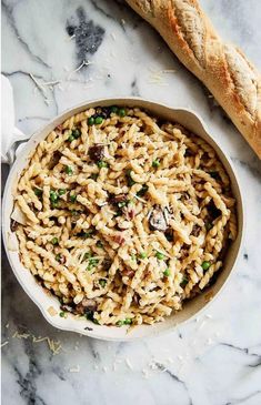 a bowl filled with pasta next to a baguette on top of a marble counter