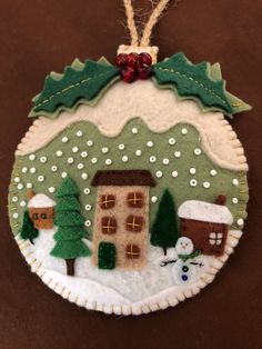 a christmas ornament hanging on a brown surface with trees and houses in the snow