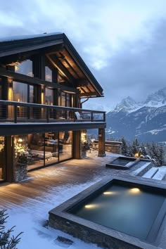 a large house with a pool in the middle of snow covered ground and mountains behind it