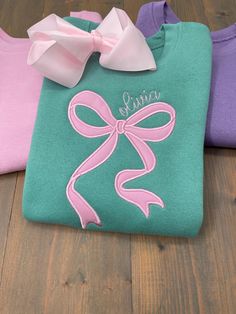 Girls Embroidered Bow Sweatshirt Make her feel special with this adorable, custom-made sweatshirt featuring a beautifully appliquéd bow with her name embroidered on the front! This cozy sweatshirt is perfect for cooler days and adds a touch of personalized style to her wardrobe. Available in fun and vibrant colors: pink, purple, navy, and seafoam green, each sweatshirt is crafted with love and attention to detail. Bow color is customizable. Light pink bow on all colors except the light pink shirt which will have a darker pink bow and name.  This personalized sweatshirt makes a wonderful gift for birthdays, holidays, or just because! Add her name, choose her favorite color, and watch her light up in excitement! Sweatshirt: *7.5 oz./yd² (US), 12.5 oz./L yd (CA), 60/40 cotton/polyester *True Pearl Stitch, Bow Silhouette, Bow Sweatshirt, Embroider Ideas, Monogram Bow, Choose Her, Light Pink Shirt, Embroidered Items