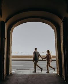 a man and woman holding hands as they walk through an archway