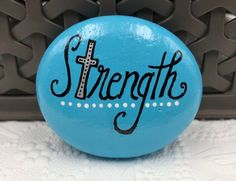 a blue button with the word strength painted on it and a cross at the bottom