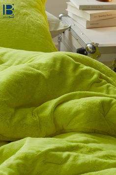 a lime green comforter on a bed next to two books and a lamp in the background