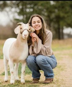 a woman kneeling down next to a goat