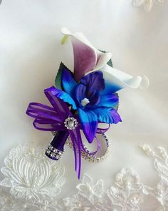 a purple and blue flower on a white lace fabric with brooches in the background