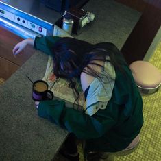 a woman sitting at a counter with her head down on a newspaper next to a cup of coffee