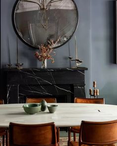 a dining room table with four chairs and a large circular mirror above the fire place