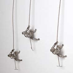 three silver necklaces hanging from chains on a white wall and one is holding a cat