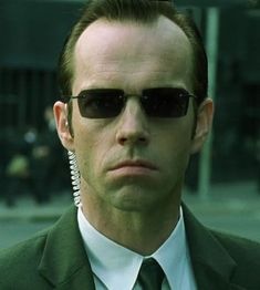 a man wearing sunglasses and a green suit is staring at the camera with his head tilted to the side