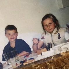 two young children sitting at a table with drinks and snacks on it, in front of a photo of them