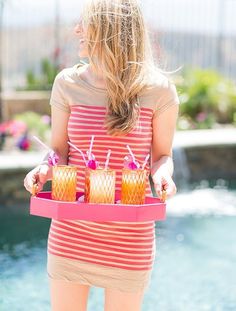 a woman holding a tray with candles in front of a pool and water fountain behind her