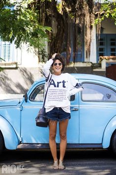 a woman standing next to an old blue car