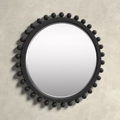 a round mirror hanging on the wall with black balls around it and an oval frame