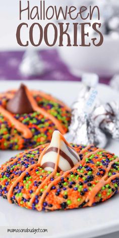 halloween cookies with candy and sprinkles on a white plate next to silver foil