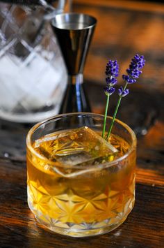 a close up of a drink in a glass on a table with ice and flowers