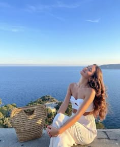 a woman sitting on the edge of a cliff with her eyes closed and looking up at the sky