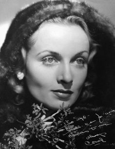 an old black and white photo of a woman with flowers in her hair, looking at the camera