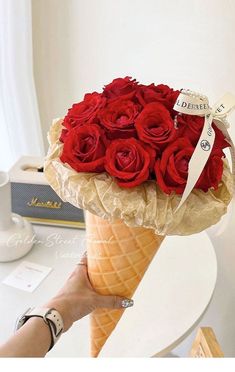 a hand holding an ice cream cone with red roses in it and a ribbon around the top