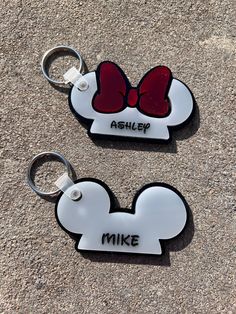 two mickey mouse keychains with red bows on them, one is white and the other is black