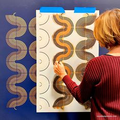 a woman is working on an art piece in front of a blue and white wall