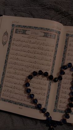 a rosary laying on top of an open book with arabic writing and blue beads hanging from it