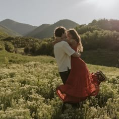 a man and woman hug in the middle of a field with mountains in the background