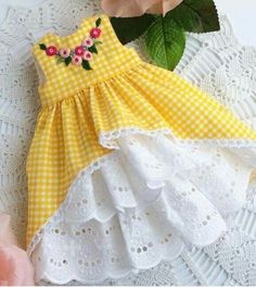 a yellow and white dress sitting on top of a lace doily next to a pink rose